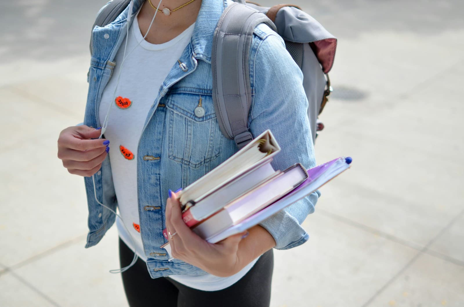 A student carrying books and a backpack outside